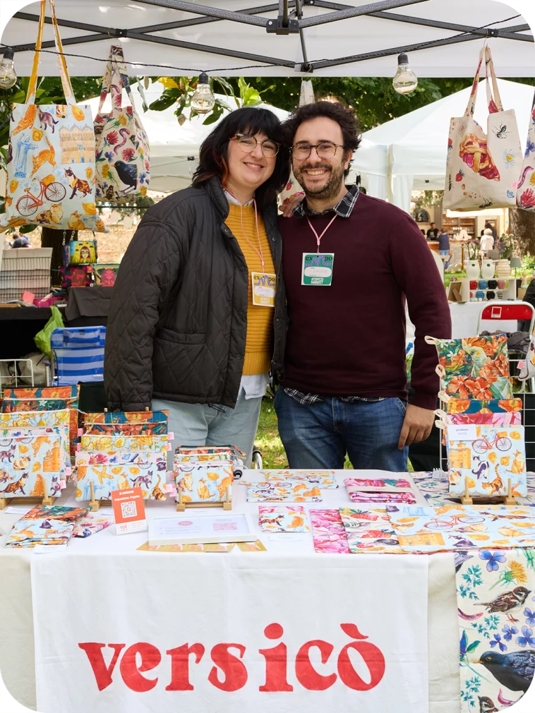 Una donna (Eleonora Spada) e un uomo (Simone Bulletti) sono in piedi al centro della foto dietro ad uno stand espositivo dei prodotti versicò durante un mercato dell'artigianato