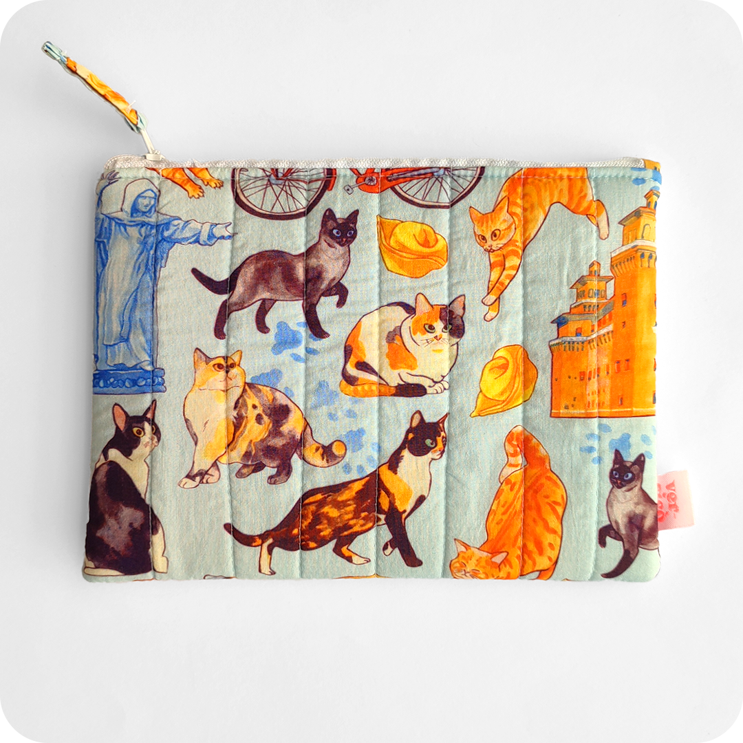 Astuccio realizzato in tessuto con gatti, cappelletti, coppie di pane e altri elementi legati a Ferrara (castello, biciclette, duomo, statua Savonarola) su sfondo azzurro