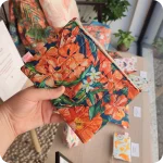 Astuccio realizzato con tessuto stampato con fiori sui toni dell'arancione e foglie bluastre