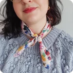 Dettaglio del collo di una donna che indossa bandana legata al collo realizzata con un tessuto in cotone stampato con chiocciole, api, coccinelle, merli, fragole, fiori e foglie su fondo rosa