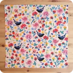 Bandana quadrata stesa sopra un tavolo in legno realizzata con un tessuto in cotone stampato con chiocciole, api, coccinelle, merli, fragole, fiori e foglie su fondo rosa