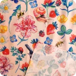 Dettaglio dell'orlo di una bandana realizzata con un tessuto in cotone stampato con chiocciole, api, coccinelle, merli, fragole, fiori e foglie su fondo rosa