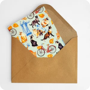 Biglietto d'auguri con gatti che saltano, biciclette, cappelletti, coppie di pane e statua del Savonarola su fondo azzurro; con busta avana