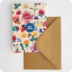 Biglietto d'auguri con il logo di Versicò al centro attorniato da fiori, foglie, coccinelle, api, farfalle e chiocciola su fondo rosa, con busta color avana