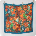 Foulard quadrato appeso realizzato con tessuto stampato con pappagalli e fiori al centro e una cornice blu