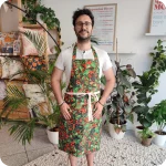 Uomo di fronte che indossa un grembiule da cucina in tessuto stampato con foglie verdi e bacche rosse e blu scuro