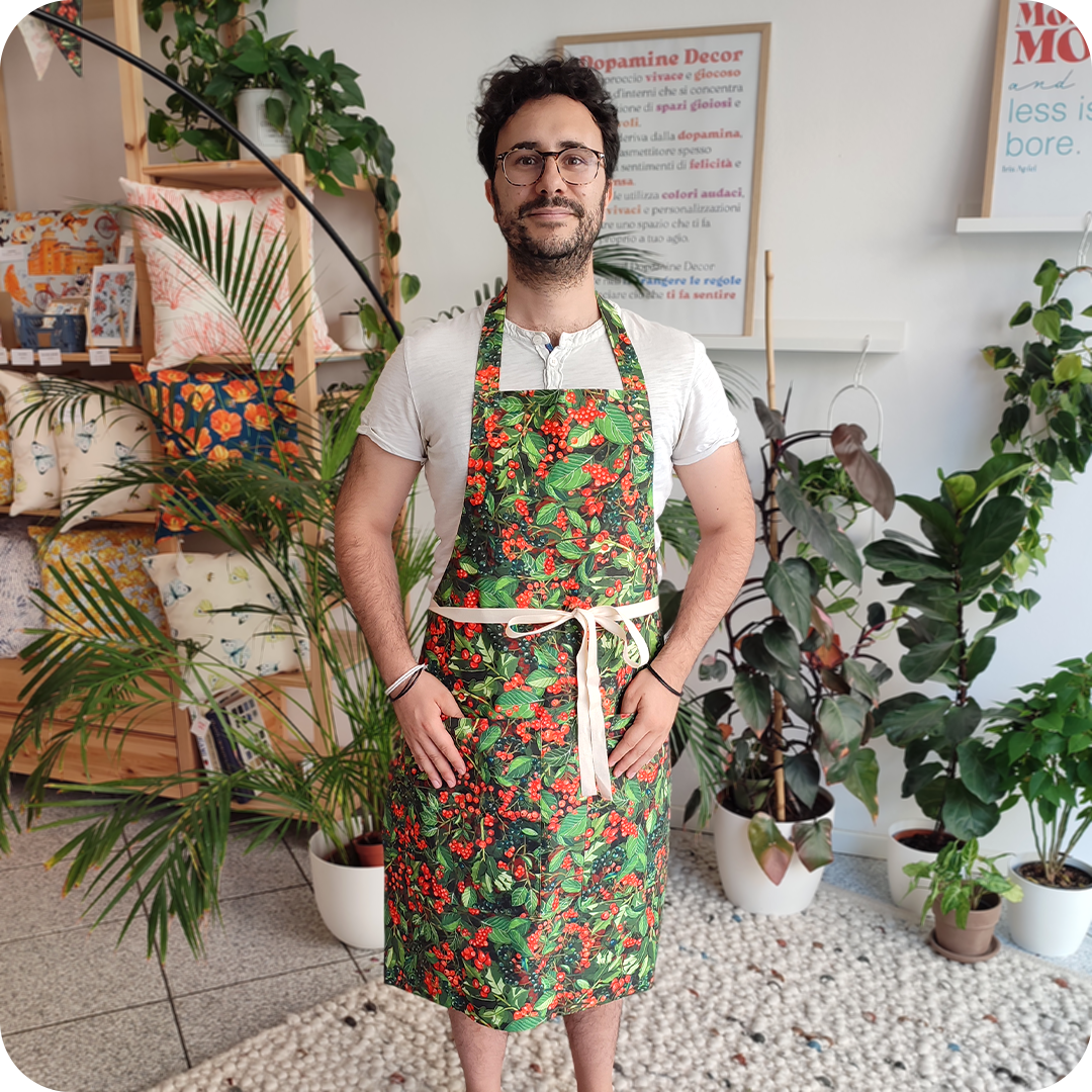 Uomo di fronte che indossa un grembiule da cucina in tessuto stampato con foglie verdi e bacche rosse e blu scuro
