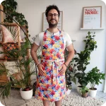 Uomo di fronte che indossa un grembiule da cucina in tessuto stampato con grandi fiori sui toni del bianco, azzurro, giallo e rosso