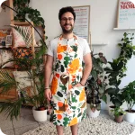 Uomo di fronte che indossa un grembiule da cucina in tessuto stampato con elementi vegetali stilizzati dai colori caldi su fondo bianco