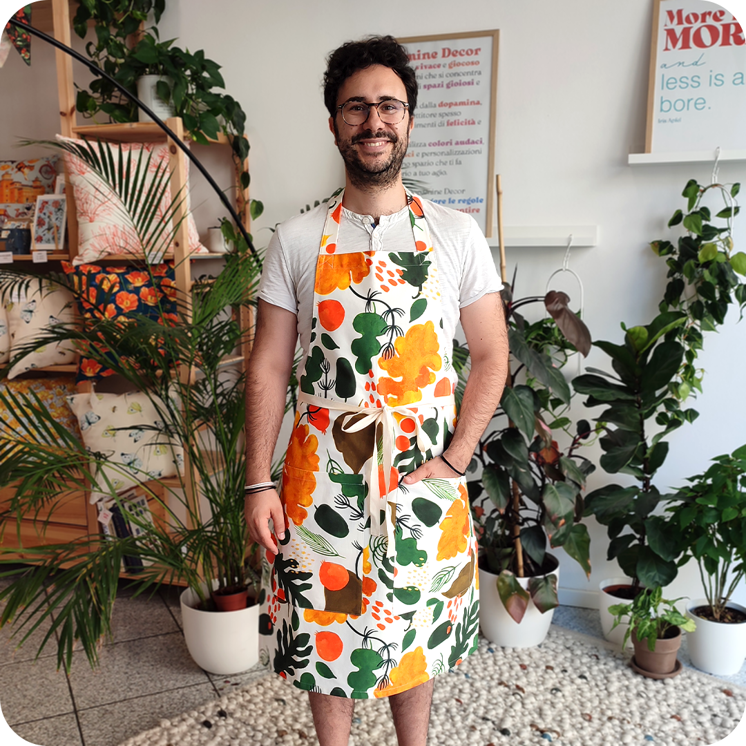 Uomo di fronte che indossa un grembiule da cucina in tessuto stampato con elementi vegetali stilizzati dai colori caldi su fondo bianco