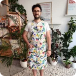 Uomo di fronte che indossa un grembiule da cucina in tessuto stampato con lucertole, fiori e foglie su fondo chiaro