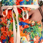 Dettaglio di un grembiule in tessuto stampato con pappagalli, falene, grilli e fiori