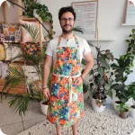 Uomo di fronte che indossa un grembiule da cucina in tessuto stampato con una fantasia jungle con pappagalli e fiori