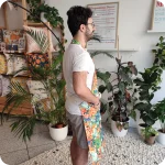 Uomo di profilo che indossa un grembiule da cucina in tessuto stampato con una fantasia jungle con pappagalli e fiori