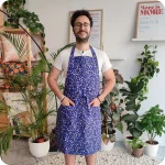 Uomo di fronte che indossa un grembiule da cucina in tessuto stampato con trifogli azzurri su un fondo blu scuro