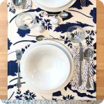 Runner apparecchiato in tessuto stampato con una fantasia con foglie blu su fondo chiaro, tovagliolo in lino abbinato con tratteggi bianchi su fondo bianco