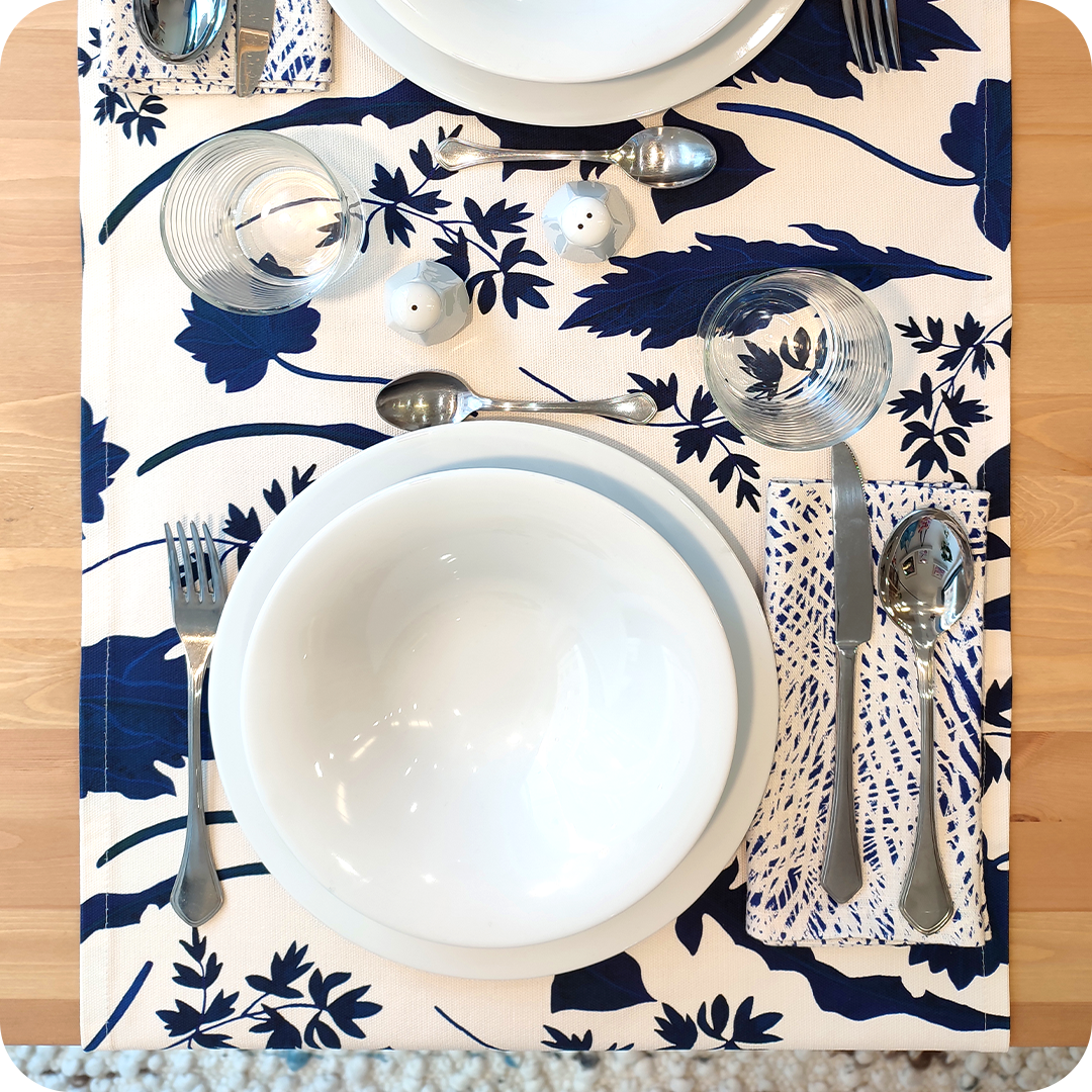 Runner apparecchiato in tessuto stampato con una fantasia con foglie blu su fondo chiaro, tovagliolo in lino abbinato con tratteggi bianchi su fondo bianco