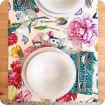 Runner apparecchiato in tessuto stampato con una fantasia con fiori, farfalle e coccinelle, tovagliolo in lino abbinato con un motivo a tratteggi verdi su fondo chiaro