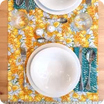 Runner apparecchiato in tessuto stampato con una fantasia con fiori gialli e bianchi, tovagliolo in lino abbinato con un motivo a tratteggi verdi su fondo chiaro