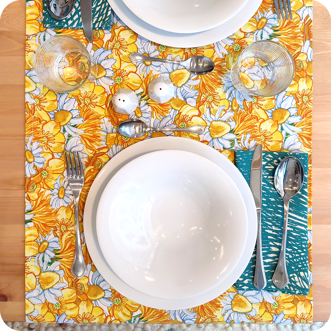 Runner apparecchiato in tessuto stampato con una fantasia con fiori gialli e bianchi, tovagliolo in lino abbinato con un motivo a tratteggi verdi su fondo chiaro