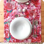 Runner apparecchiato realizzato con un tessuto stampato con disegni di garofani sui toni del rosa e del magenta con tovagliolo in tinta