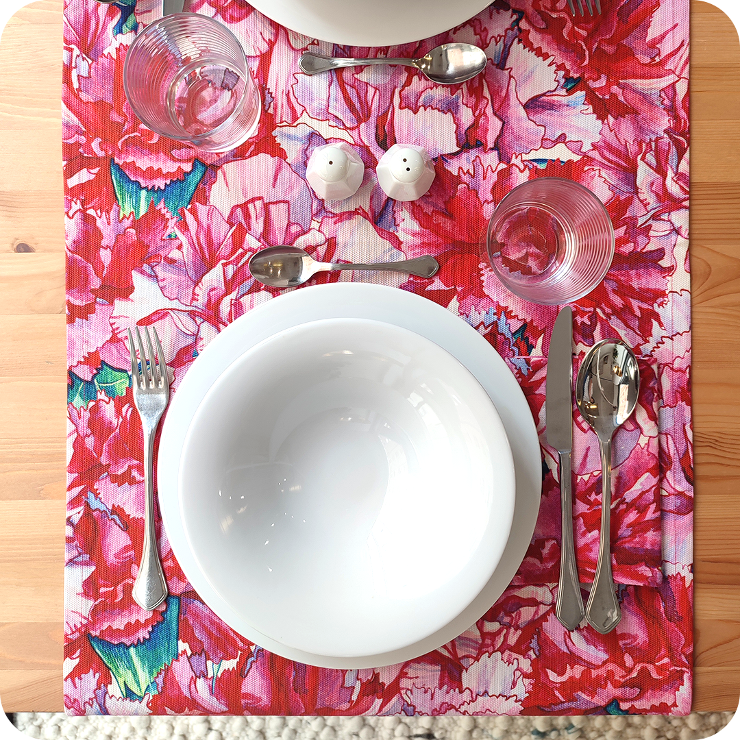 Runner apparecchiato realizzato con un tessuto stampato con disegni di garofani sui toni del rosa e del magenta con tovagliolo in tinta