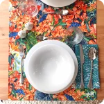 Runner apparecchiato realizzato con un tessuto stampato con pappagalli che sbucano da un fitto cespuglio fiorito su cui si poggiano qua e là grilli e falene, con tovagliolo abbinato bianco e verde