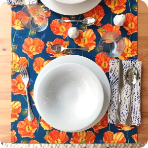 Runner apparecchiato realizzato con un tessuto stampato con papaveri, falene, lucciole e grilli su fondo blu, con tovagliolo abbinato bianco e blu