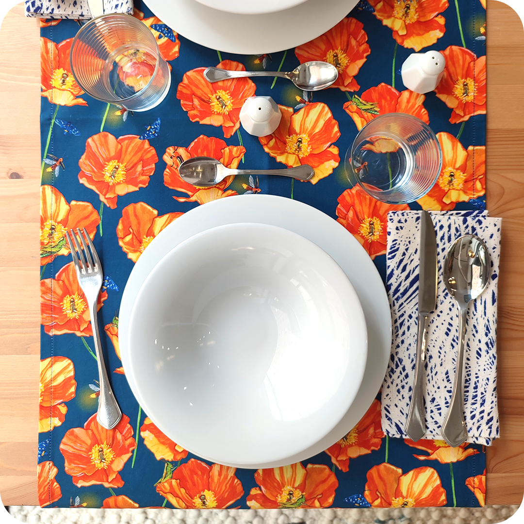 Runner apparecchiato realizzato con un tessuto stampato con papaveri, falene, lucciole e grilli su fondo blu, con tovagliolo abbinato bianco e blu