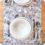 Runner apparecchiato in tessuto stampato con una fantasia a tratteggi bianchi su fondo blu, tovagliolo abbinato in lino