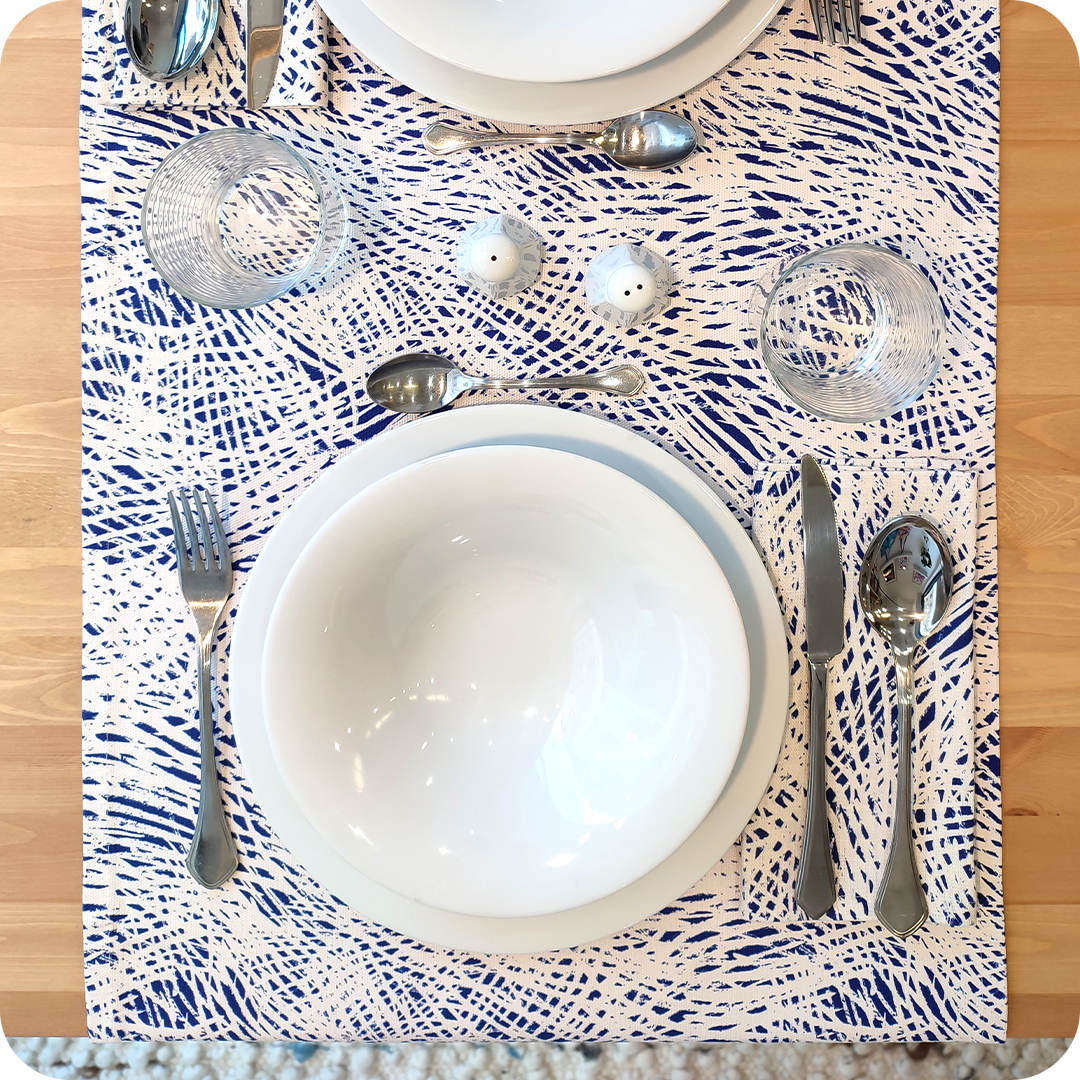Runner apparecchiato in tessuto stampato con una fantasia a tratteggi bianchi su fondo blu, tovagliolo abbinato in lino