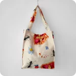 Borsa in tessuto stampato con una fantasia con fette di crostata, formiche, fiori e fragole su fondo chiaro