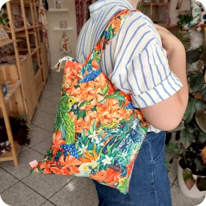 Donna che indossa su una spalla una borsa con cerniera in tessuto stampato con una fantasia jungle con pappagalli e falene che sbucano tra fiori e foglie