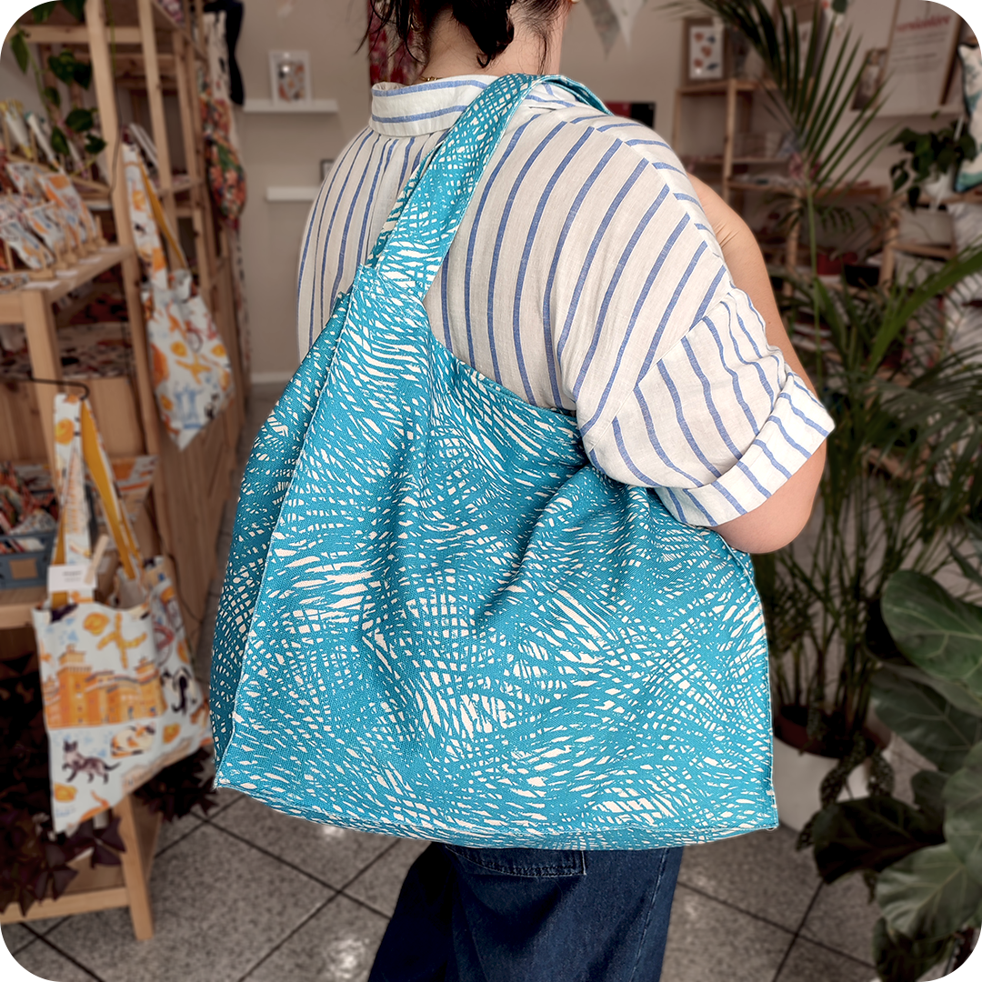 Donna che indossa su una spalla una grande borsa in tessuto stampato con un motivo a tratteggio azzurro su fondo bianco