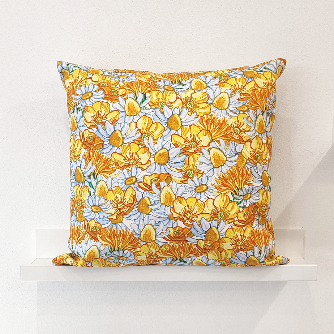 Cuscino quadrato realizzato con un tessuto in cotone stampato con fiori gialli e bianchi, tra cui ranuncoli selvatici, margherite, camomilla, tarassaco
