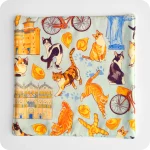 Sottopentola in tessuto imbottito realizzato con una stoffa stampata con gatti, cappelletti, coppie di pane, biciclette, duomo e castello di Ferrara su fondo azzurro