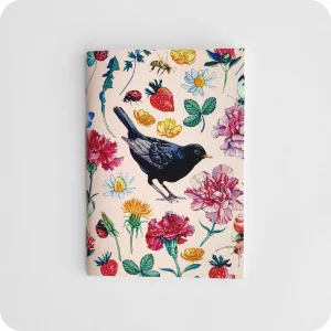 Fronte di un taccuino decorato con un merlo al centro attorniato da fiori, fragole, coccinelle, api su un fondo rosa
