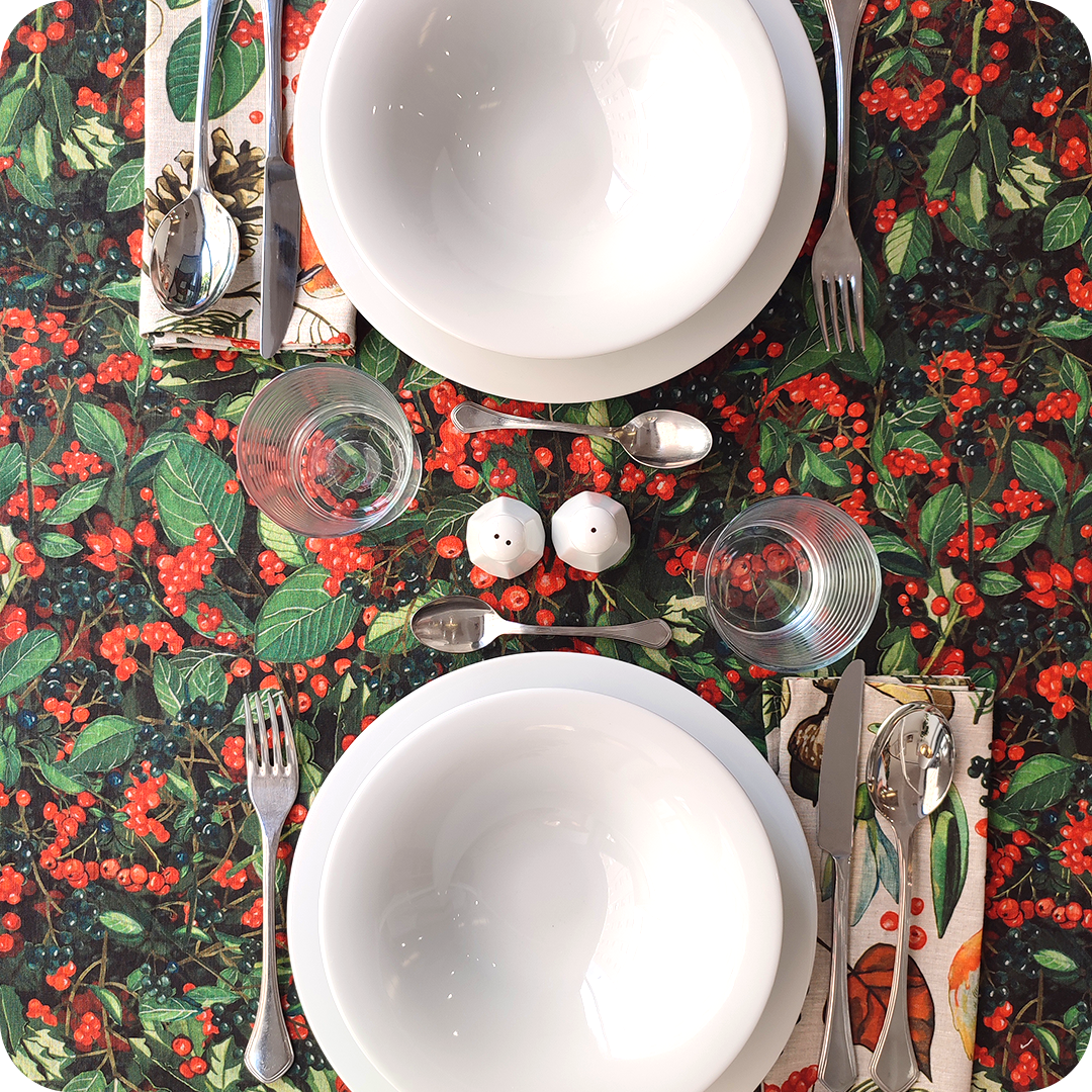 Tovaglia apparecchiata realizzata con un tessuto in lino naturale stampato con una fantasia con bacche rosse e scure e foglie verdi