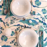 Tovaglia apparecchiata realizzata in tessuto stampato con foglie verdi azzurre su fondo chiaro; tovaglioli abbinati con un motivo a tratteggi verdi su fondo chiaro