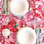 Tovaglia apparecchiata realizzata in tessuto stampato con garofani rosa e magenta; tovaglioli abbinati con motivo a tratteggi bianchi su fondo blu