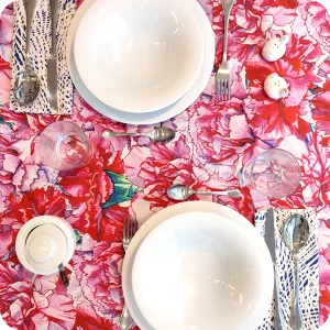 Tovaglia apparecchiata realizzata in tessuto stampato con garofani rosa e magenta; tovaglioli abbinati con motivo a tratteggi bianchi su fondo blu