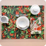 Tovaglietta rettangolare apparecchiata realizzata con un tessuto stampato con una fantasia con bacche e foglie; tovagliolo in lino abbinato