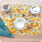 Tovaglietta rettangolare apparecchiata realizzata con un tessuto stampato con una fantasia fiori bianchi e gialli; tovagliolo in lino abbinato stampato con un motivo a tratteggi verdi su fondo chiaro