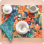 Tovaglietta rettangolare apparecchiata realizzata con un tessuto stampato con una fantasia con pappagalli, falene, grilli che sbucano da un cespuglio di fiori; tovagliolo in lino abbinato con motivo a tratteggio verde e bianco