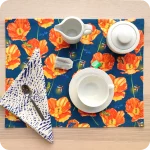 Tovaglietta rettangolare apparecchiata realizzata con un tessuto stampato con una fantasia con papaveri, lucciole, falene, grilli su fondo blu; tovagliolo in lino abbinato stampato con motivo a tratteggio bianco e blu
