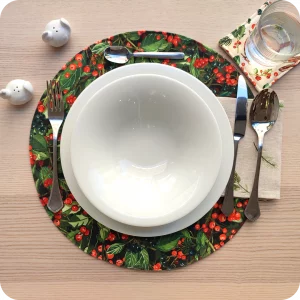 Tovaglietta tonda apparecchiata realizzata in tessuto stampato con una fantasia con bacche e foglie; tovagliolo abbinato in lino écru con pattern di rametti di pino e pigne
