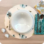 Tovaglietta tonda realizzata in tessuto stampato con fantasia fiori bianchi e gialli; tovagliolo in lino abbinato con motivo a tratteggio verde su fondo bianco