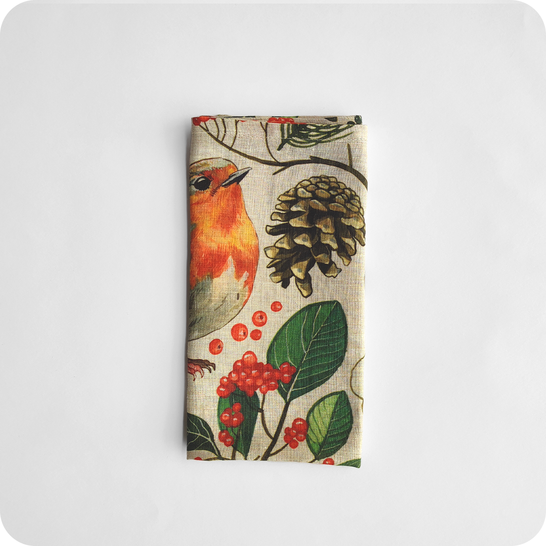 Tovagliolo quadrato piegato in lino écru stampato con una fantasia di pettirossi, pigne, rametti, fiori, funghi, ghiande, bacche, foglie