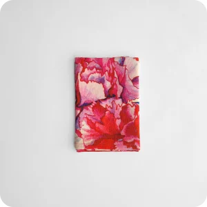 Tovagliolo piegato in tessuto stampato con una fantasia di garofani sui toni del rosa e del magenta