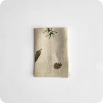 Tovagliolo quadrato piegato in lino écru stampato con una fantasia di rametti di pino e pigne